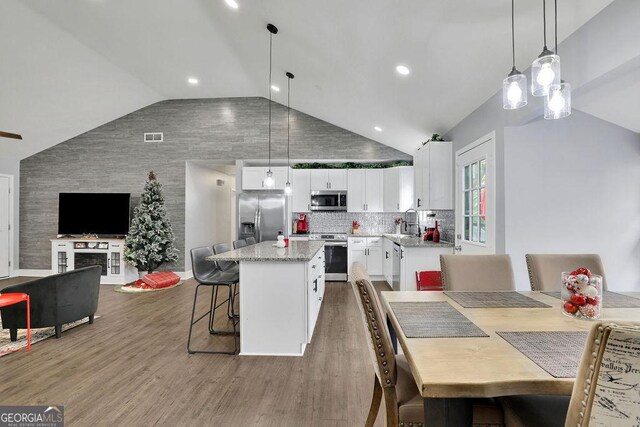 kitchen featuring vaulted ceiling, appliances with stainless steel finishes, light stone counters, a kitchen island, and white cabinets