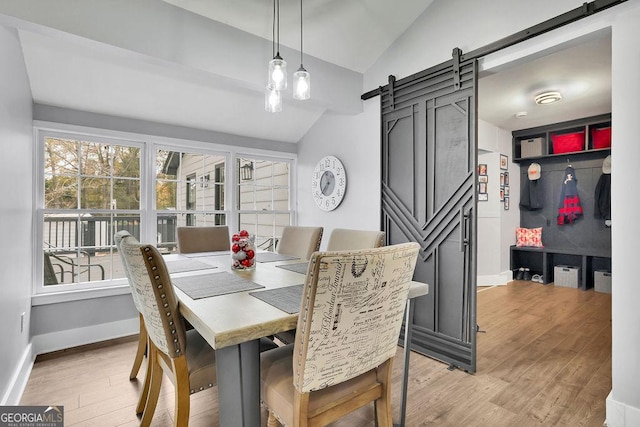 dining area featuring lofted ceiling, light wood-type flooring, and a barn door