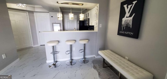 kitchen with a kitchen bar, kitchen peninsula, white cabinetry, and hanging light fixtures