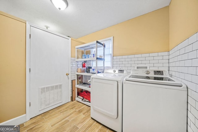 laundry area featuring separate washer and dryer, light hardwood / wood-style flooring, and a textured ceiling