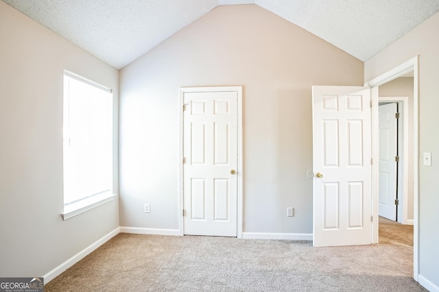 unfurnished bedroom featuring light colored carpet, lofted ceiling, and a textured ceiling