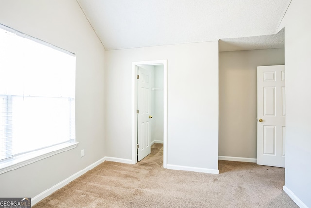 unfurnished bedroom with a textured ceiling, a spacious closet, light colored carpet, and vaulted ceiling