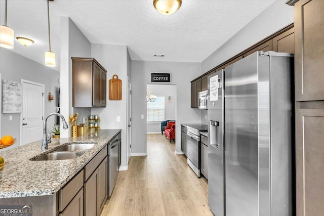 kitchen with pendant lighting, sink, a textured ceiling, appliances with stainless steel finishes, and light stone counters