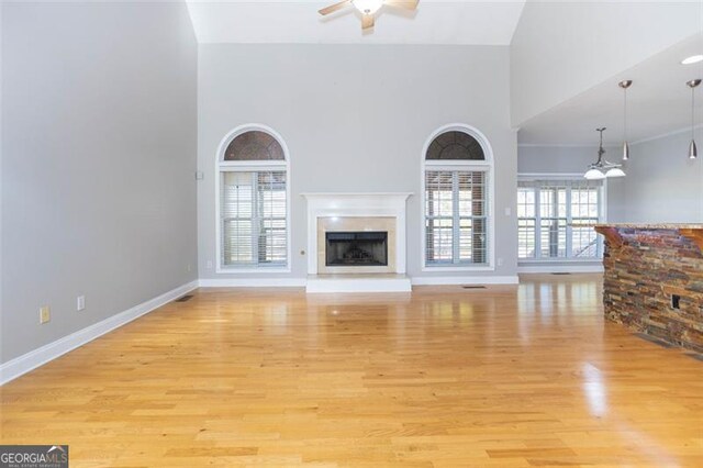 unfurnished living room with ceiling fan, light wood-type flooring, and a high ceiling