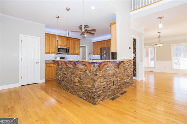 kitchen with sink, stainless steel appliances, crown molding, decorative light fixtures, and light wood-type flooring