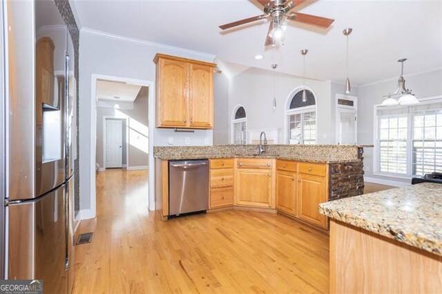 kitchen with light stone counters, stainless steel appliances, ceiling fan, sink, and decorative light fixtures