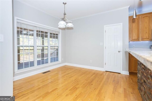 unfurnished dining area with a chandelier, light hardwood / wood-style flooring, and crown molding