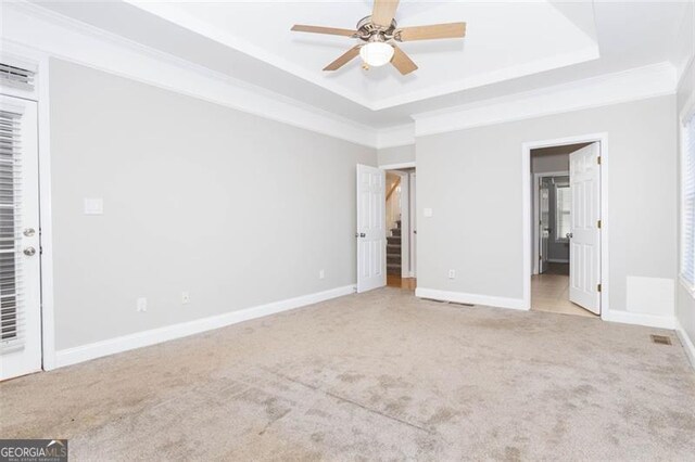 unfurnished bedroom with ceiling fan, light colored carpet, and a tray ceiling