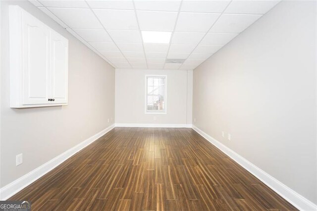 empty room with a drop ceiling and dark wood-type flooring