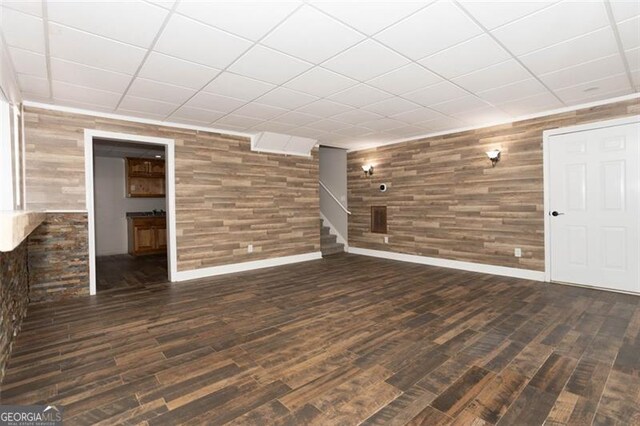 basement featuring a drop ceiling, dark wood-type flooring, and wooden walls