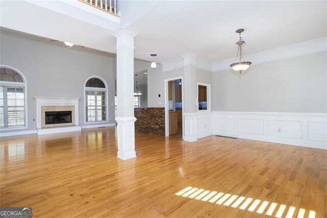 unfurnished living room featuring light wood-type flooring, decorative columns, plenty of natural light, and crown molding