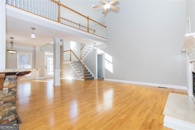 unfurnished living room with ornate columns, a fireplace, a towering ceiling, and light wood-type flooring