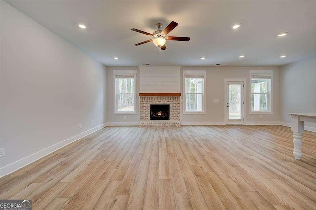 unfurnished living room featuring a brick fireplace, ceiling fan, a healthy amount of sunlight, and light hardwood / wood-style floors