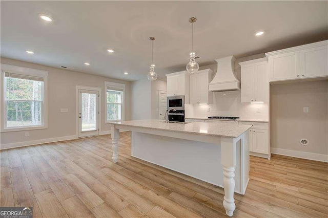 kitchen featuring appliances with stainless steel finishes, custom exhaust hood, pendant lighting, a center island with sink, and white cabinets