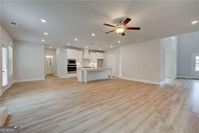 kitchen featuring white cabinetry, sink, stainless steel microwave, a kitchen island with sink, and custom exhaust hood