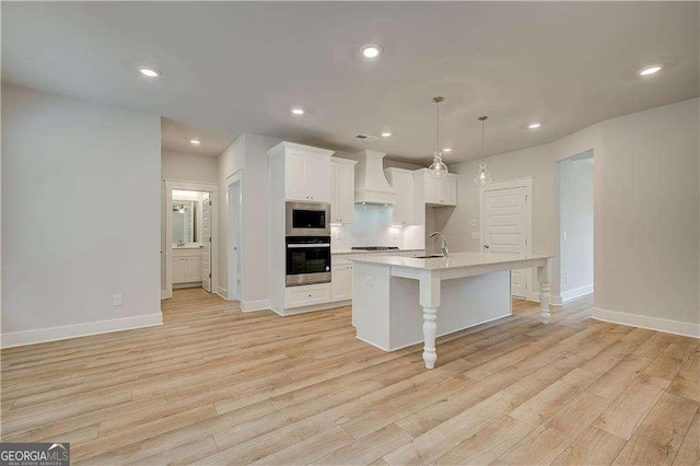 kitchen with a kitchen island with sink, light hardwood / wood-style flooring, custom exhaust hood, and appliances with stainless steel finishes