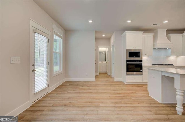 kitchen with appliances with stainless steel finishes, tasteful backsplash, custom exhaust hood, light hardwood / wood-style flooring, and white cabinets