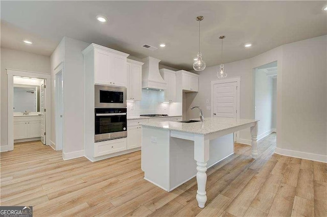 kitchen featuring white cabinetry, stainless steel appliances, a kitchen island with sink, custom range hood, and light wood-type flooring