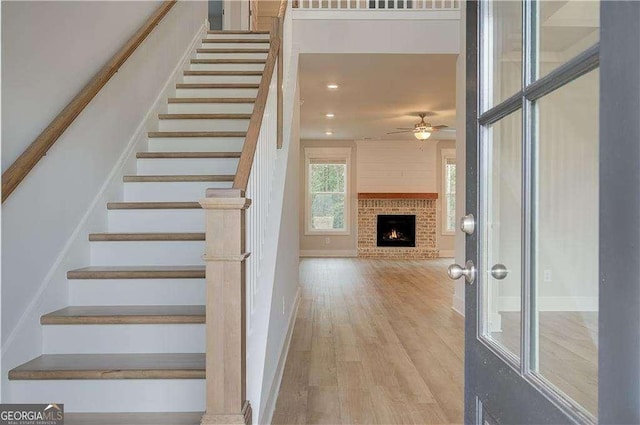 staircase with hardwood / wood-style flooring, a brick fireplace, and ceiling fan