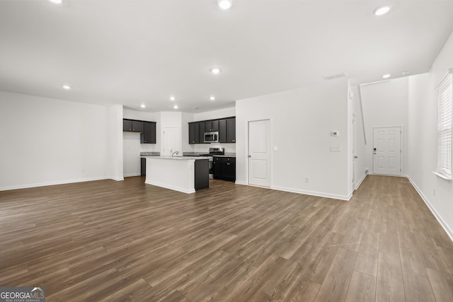 kitchen with light stone counters, a center island with sink, dark wood-type flooring, and appliances with stainless steel finishes