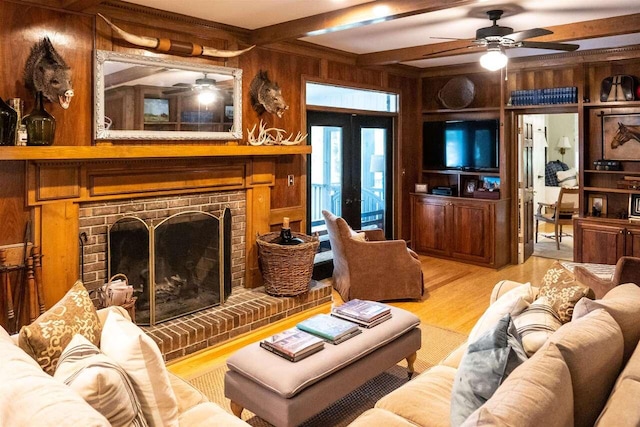 living room featuring wood walls, french doors, a fireplace, beamed ceiling, and light hardwood / wood-style floors