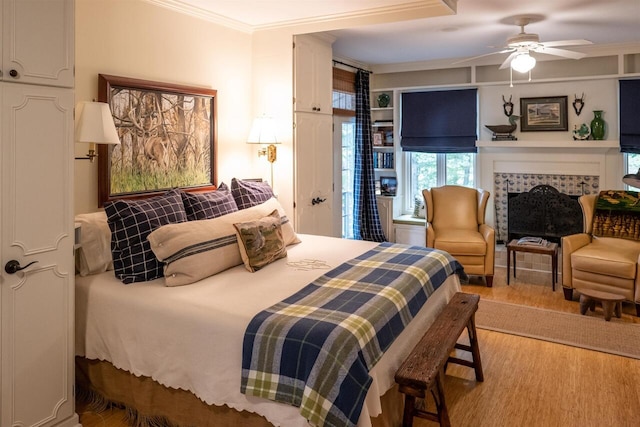 bedroom with a tile fireplace, hardwood / wood-style flooring, ceiling fan, and crown molding