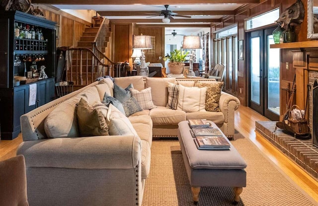 living room featuring wood walls, french doors, ceiling fan, light wood-type flooring, and beamed ceiling