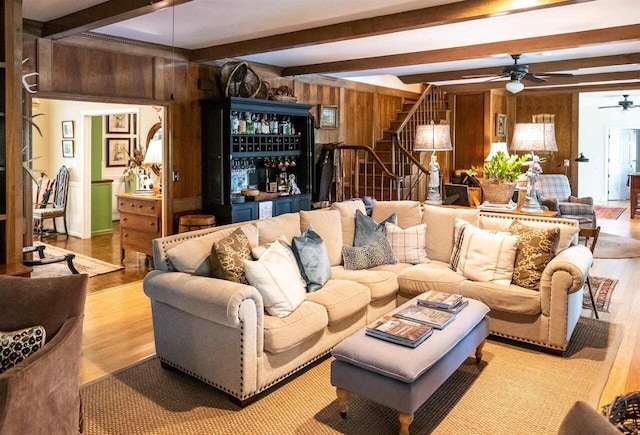 living room featuring beamed ceiling, ceiling fan, wood walls, and light hardwood / wood-style flooring