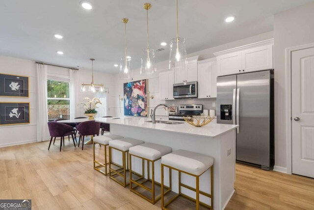 kitchen featuring a kitchen breakfast bar, stainless steel appliances, decorative light fixtures, white cabinetry, and an island with sink