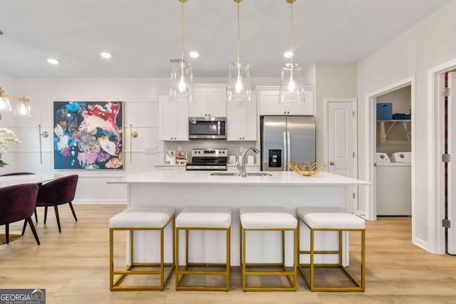 kitchen featuring a kitchen bar, appliances with stainless steel finishes, a kitchen island with sink, sink, and white cabinets