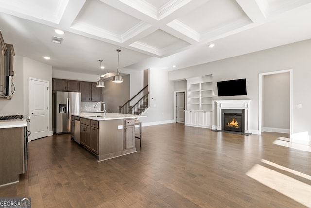 kitchen with appliances with stainless steel finishes, coffered ceiling, pendant lighting, a center island with sink, and beamed ceiling