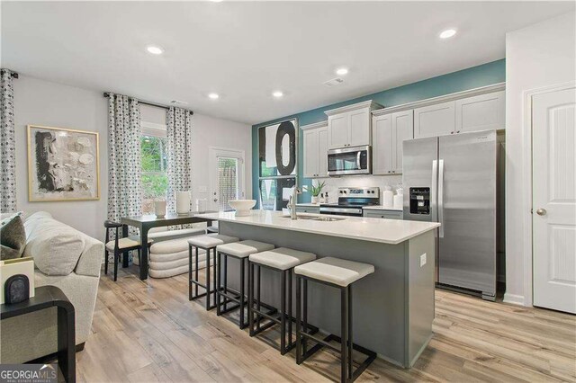 kitchen with sink, a breakfast bar area, an island with sink, white cabinetry, and stainless steel appliances