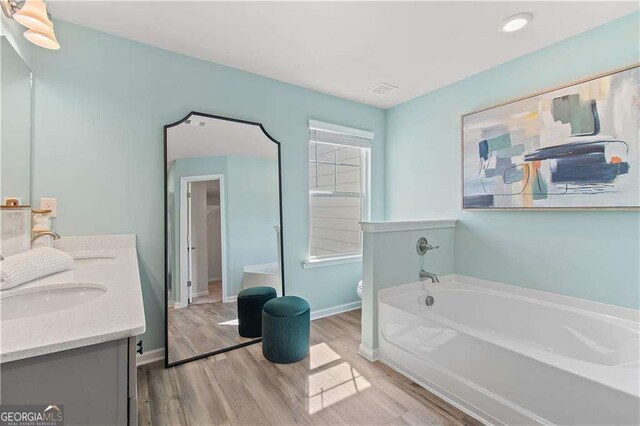 bathroom featuring a washtub, hardwood / wood-style floors, vanity, and toilet