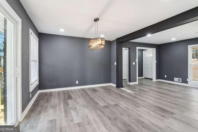 unfurnished dining area featuring beam ceiling, an inviting chandelier, and light wood-type flooring