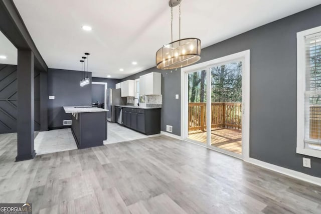 kitchen with pendant lighting, white cabinets, light hardwood / wood-style floors, appliances with stainless steel finishes, and a kitchen island