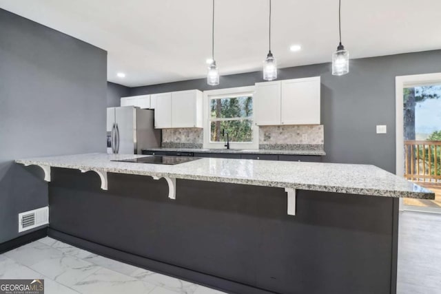 kitchen with white cabinets, stainless steel fridge, backsplash, and decorative light fixtures