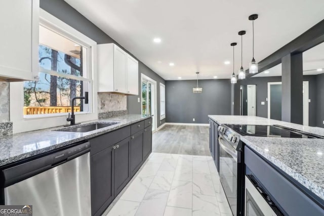 kitchen featuring hanging light fixtures, light stone counters, decorative backsplash, white cabinets, and appliances with stainless steel finishes