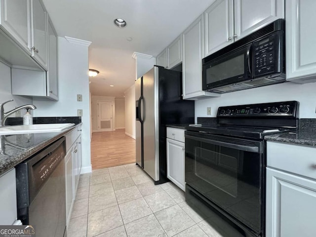 kitchen with sink, black appliances, light tile patterned floors, dark stone countertops, and white cabinets