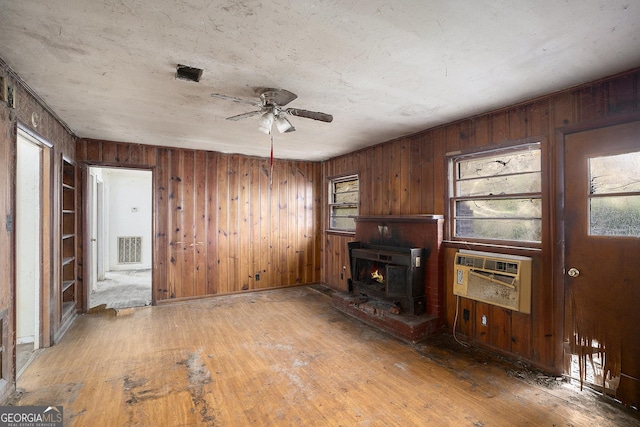 unfurnished living room with wood-type flooring, a wood stove, ceiling fan, and a wall unit AC