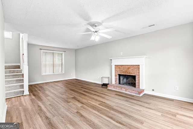 unfurnished living room with a textured ceiling, ceiling fan, light hardwood / wood-style floors, and a fireplace