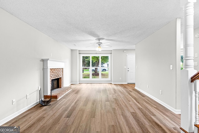 unfurnished living room featuring ceiling fan, a fireplace, a textured ceiling, and light hardwood / wood-style flooring