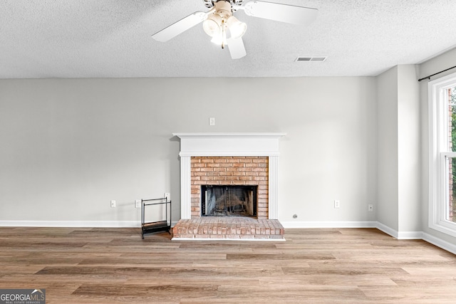 unfurnished living room with ceiling fan, light hardwood / wood-style flooring, a textured ceiling, and a brick fireplace