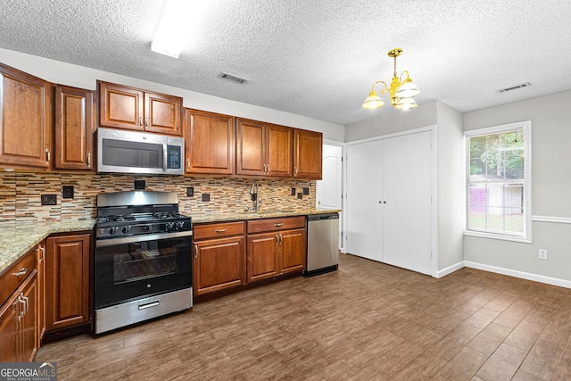 kitchen with light stone countertops, appliances with stainless steel finishes, sink, an inviting chandelier, and hanging light fixtures