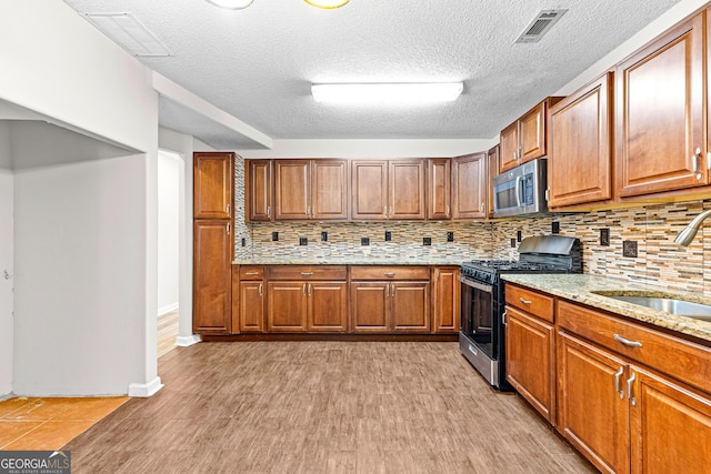 kitchen featuring light stone countertops, appliances with stainless steel finishes, tasteful backsplash, sink, and light hardwood / wood-style flooring