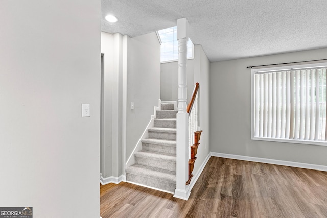 stairs featuring a wealth of natural light, hardwood / wood-style floors, and a textured ceiling