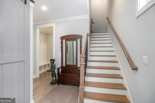 stairway with a barn door, hardwood / wood-style floors, and ornamental molding