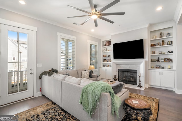 living room with built in shelves, ceiling fan, a high end fireplace, hardwood / wood-style flooring, and ornamental molding