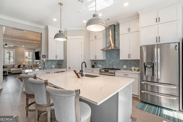 kitchen with a kitchen island with sink, sink, wall chimney exhaust hood, light stone counters, and stainless steel appliances