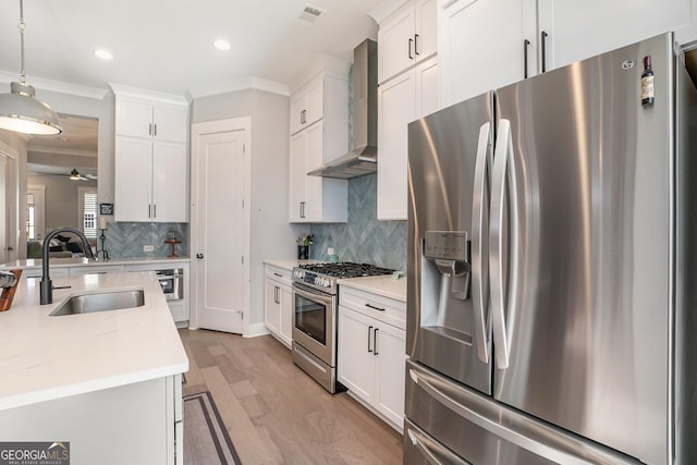 kitchen with sink, wall chimney range hood, pendant lighting, white cabinets, and appliances with stainless steel finishes