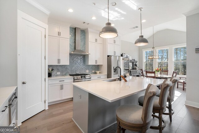 kitchen featuring lofted ceiling, decorative light fixtures, a kitchen island with sink, and wall chimney exhaust hood